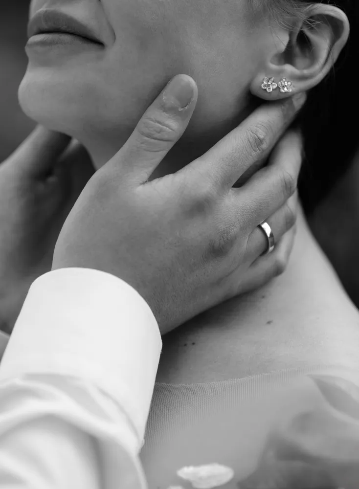 Man in suit gently touches woman's face, highlighting her earring. Intimate moment captured in black and white.