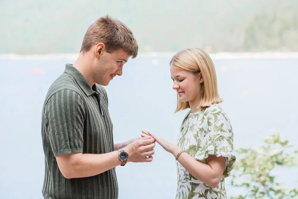 Couple standing outdoors, man in green striped polo, woman in floral dress, holding hands, natural light, serene background.