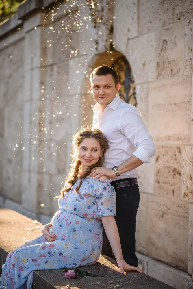 Couple in a floral dress and white shirt pose against a stone wall, sunlight and bubbles around them, conveying joy and intimacy.