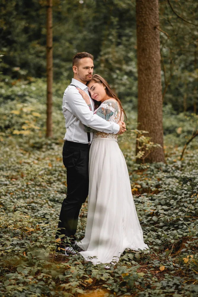 Couple in wedding attire embracing in a serene forest setting.