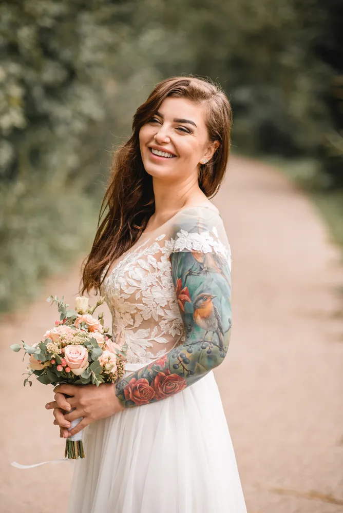 Woman in white wedding dress holds bouquet on a path surrounded by greenery.