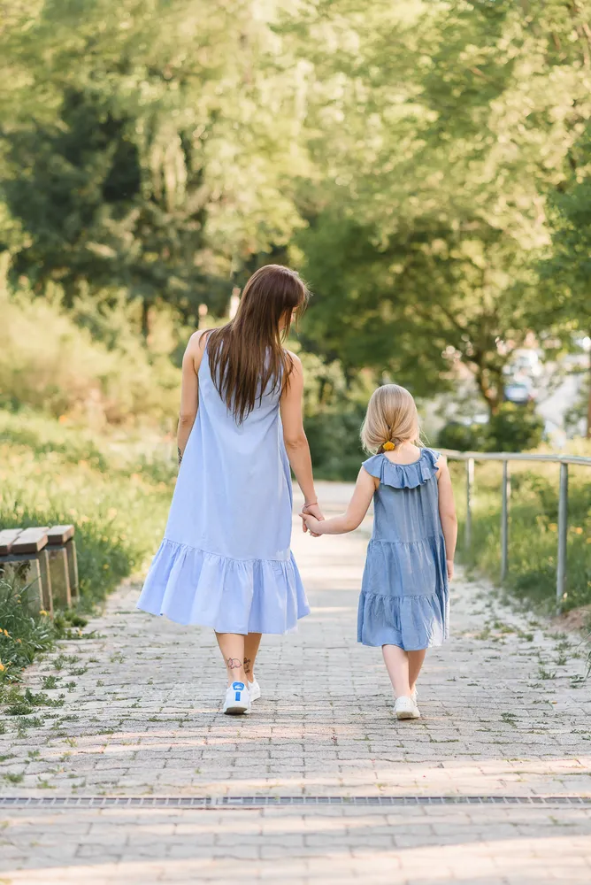 Two women in matching light blue dresses walk hand in hand down a cobblestone path surrounded by lush greenery, creating a serene and picturesque scene.