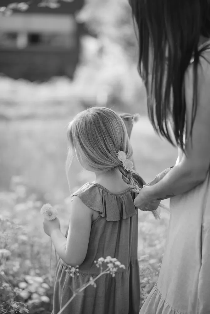 Woman braiding flowers into young girl's hair in a field. Black and white photo.